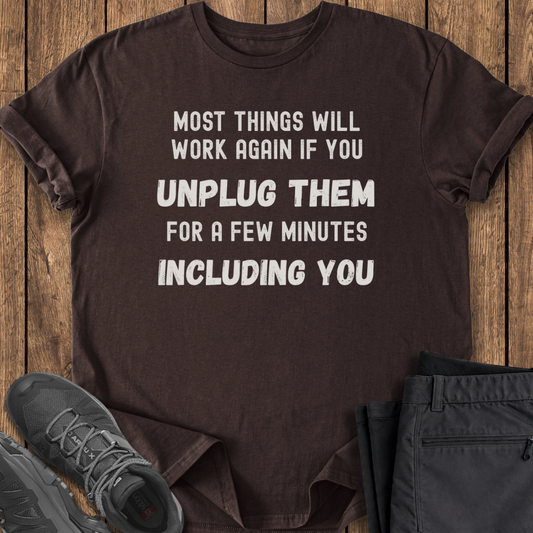 Brown t-shirt with humorous text on a wooden surface with shoes and pants.