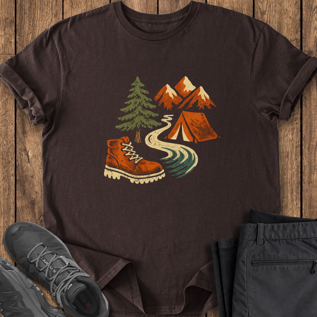 Brown t-shirt with outdoor design featuring a boot, tent, and mountains on a wooden surface.