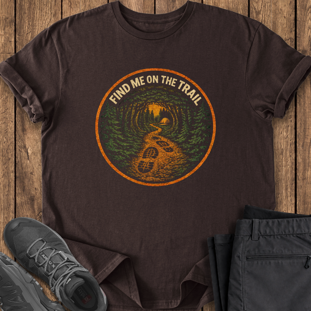 Brown t-shirt with 'Find Me on the Trail' graphic on a wooden surface with shoes and pants. hiking t shirt
