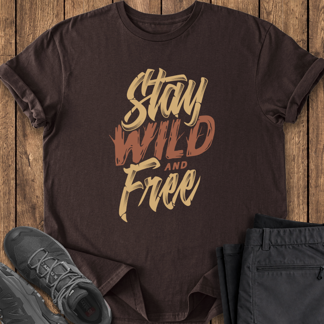 Brown t-shirt with 'Stay Wild and Free' text on a wooden surface with shoes and pants.