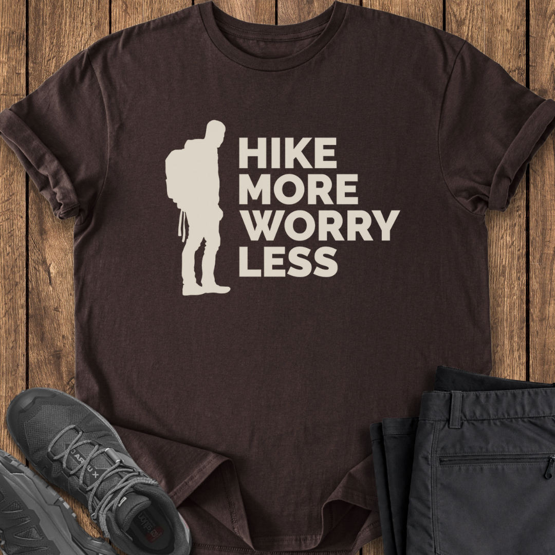 Brown t-shirt with 'Hike More Worry Less' graphic on a wooden surface with shoes and pants.