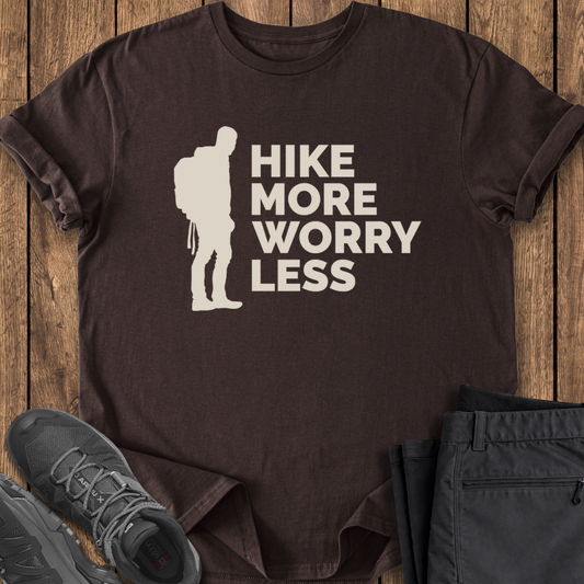 Brown t-shirt with 'Hike More Worry Less' graphic on a wooden surface with shoes and pants.