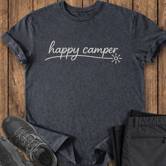 Dark gray t-shirt with 'happy camper' text on a wooden surface, accompanied by black shoes and pants.