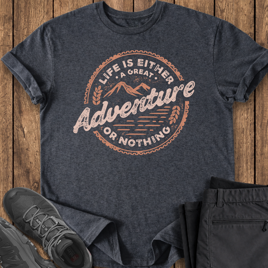 Dark gray t-shirt with 'Life is Either a Great Adventure or Nothing' text on a wooden surface, with black shoes and pants.