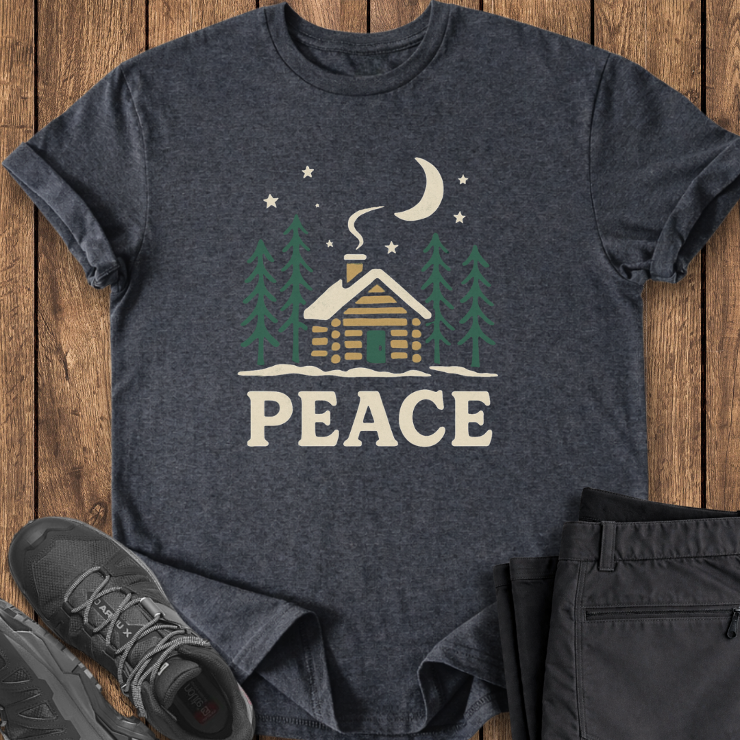 Dark gray t-shirt with a cabin and 'PEACE' text design on a wooden surface, with shoes and pants partially visible.