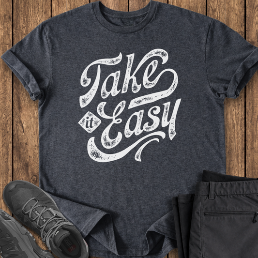 Dark gray t-shirt with 'Take It Easy' text on a wooden surface with shoes and pants.