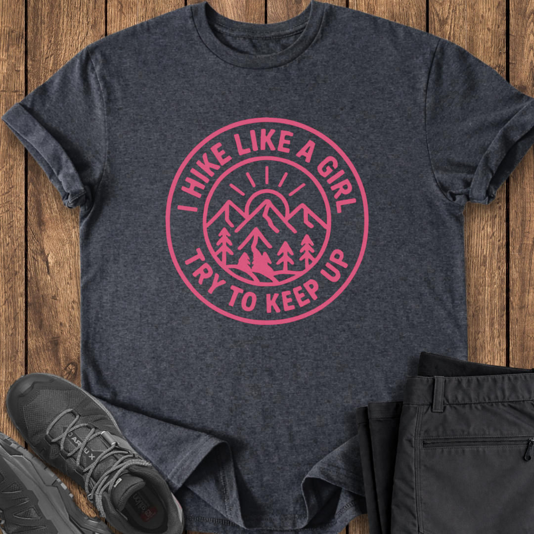 Dark gray t-shirt with pink graphic and text on a wooden surface, accompanied by black pants and shoes.