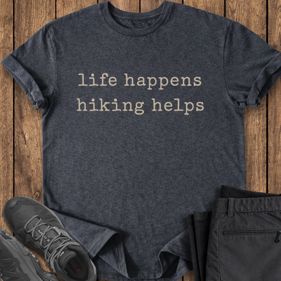 Dark gray t-shirt with 'life happens hiking helps' text on a wooden surface, with hiking shoes and pants.