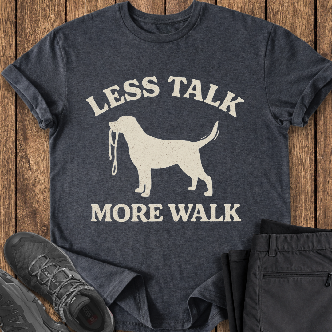 Dark gray t-shirt with a dog graphic and text 'LESS TALK MORE WALK' on a wooden surface.