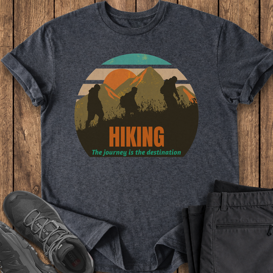 Dark gray t-shirt with hiking graphic and text on a wooden surface, accompanied by black pants and hiking shoes. three hikers mountains sunset hiking mountain t shirt
