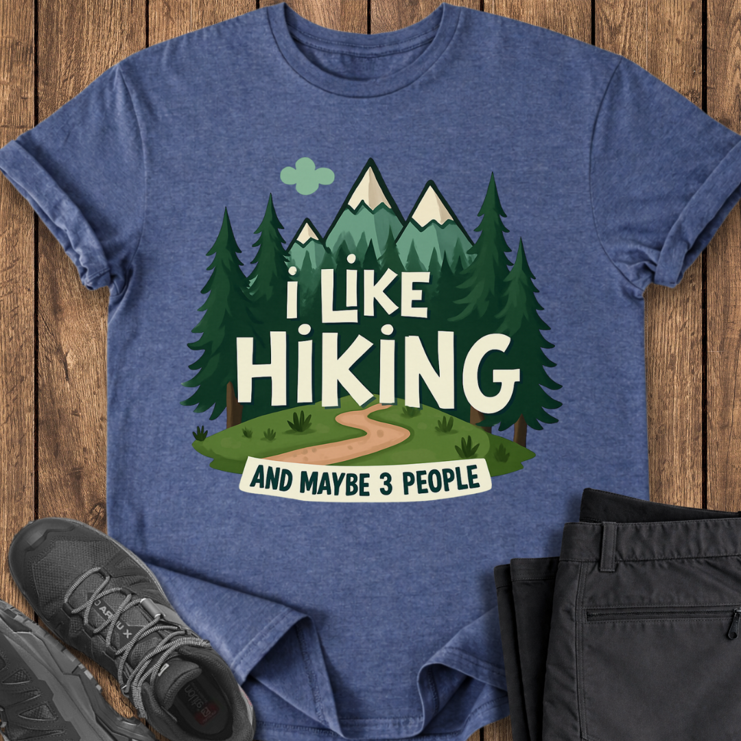 Blue t-shirt with 'I Like Hiking and Maybe 3 People' design on a wooden surface with shoes and pants.