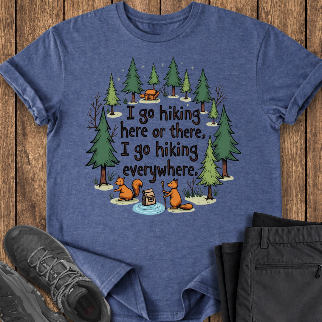 Blue t-shirt with hiking-themed design on a wooden surface with shoes and pants.