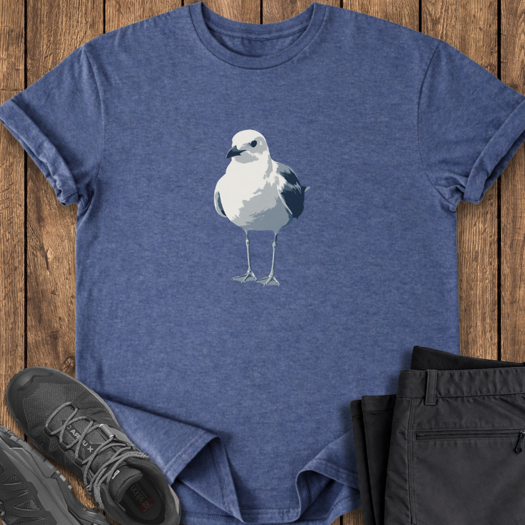 Blue t-shirt with a seagull design on a wooden surface, surrounded by black pants and shoes.