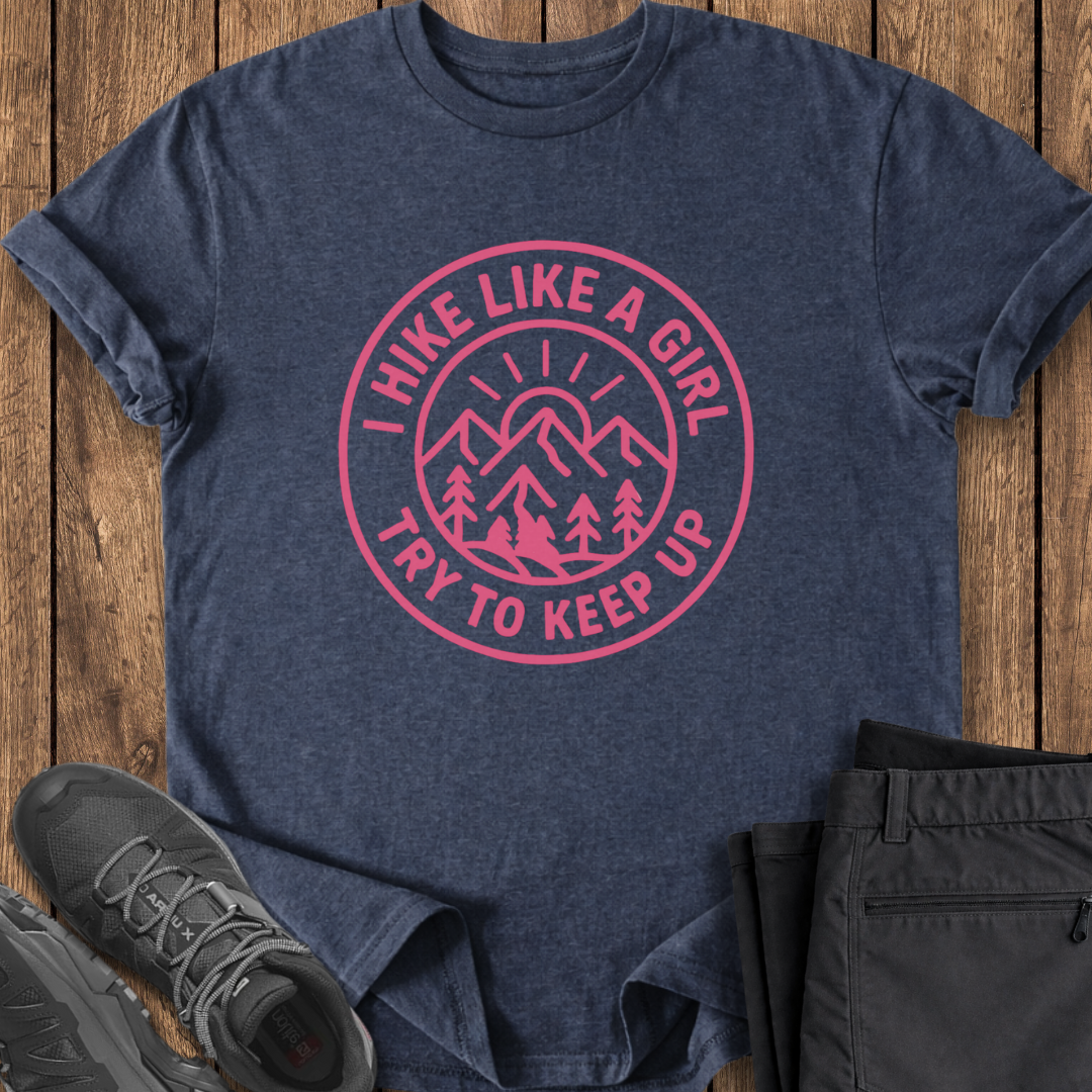 Navy t-shirt with pink graphic and text on a wooden surface, accompanied by black pants and shoes.