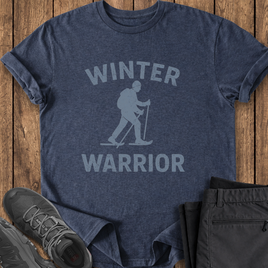 Navy blue t-shirt with 'Winter Warrior' graphic on a wooden surface, surrounded by black pants and shoes.