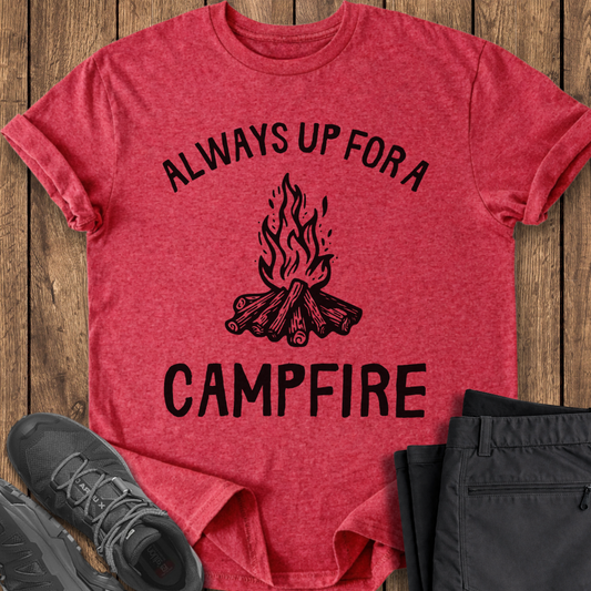 Red t-shirt with 'Always Up For a Campfire' text and graphic on a wooden surface with shoes and pants. camp camping shirt