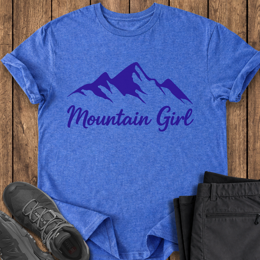 Blue t-shirt with 'Mountain Girl' text and mountain graphic on a wooden surface, with black pants and shoes.