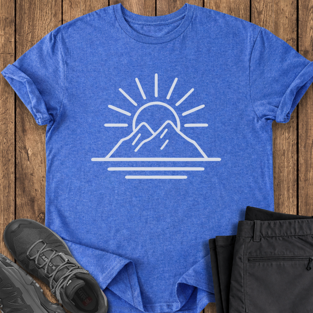Blue t-shirt with mountain and sun design on a wooden surface with shoes and pants.