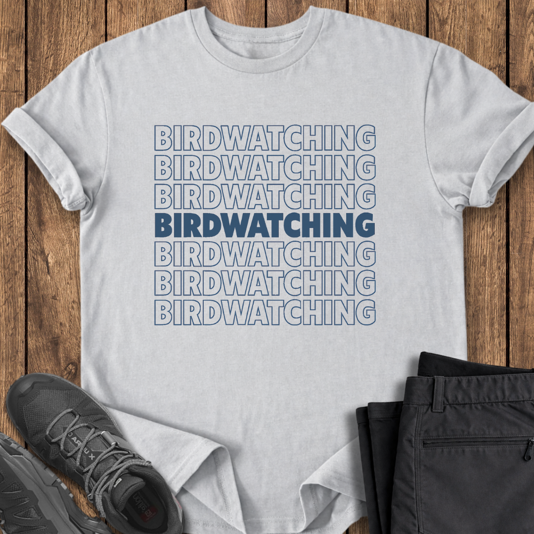 White t-shirt with 'BIRDWATCHING' text on a wooden surface with shoes and pants.