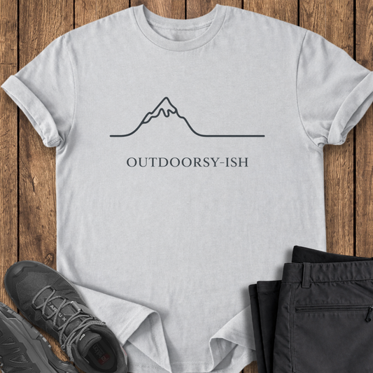 White t-shirt with mountain graphic and 'OUTDOORSY-ISH' text on a wooden surface with shoes and pants. funny minimalist mountain shirt