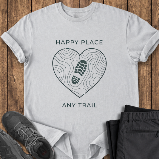 White t-shirt with 'Happy Place, Any Trail' design on a wooden surface with shoes and pants. mindfulness hiking t shirt