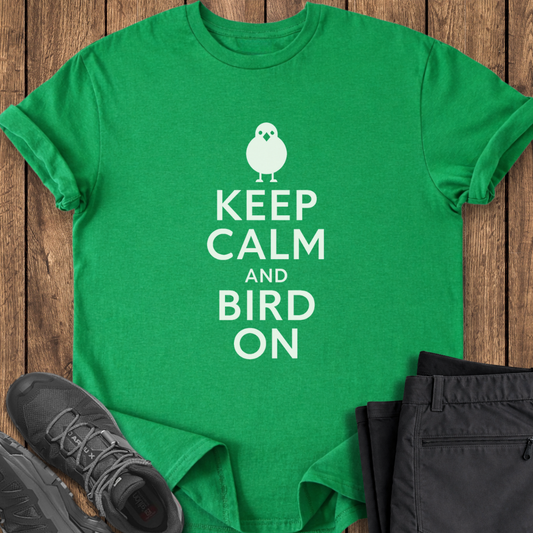 Green t-shirt with 'Keep Calm and Bird On' text on a wooden surface with black shoes and pants.