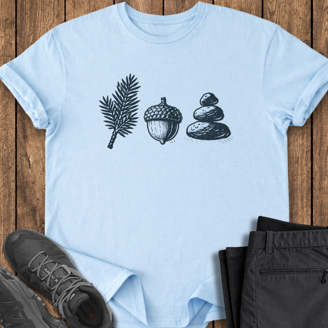 Light blue t-shirt with nature-themed design on a wooden surface with shoes and pants. hiking camping t shirt