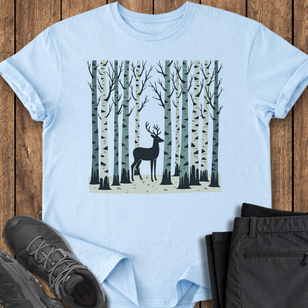 Light blue t-shirt with a deer in a forest design on a wooden surface with shoes and pants.