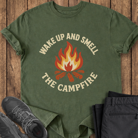Green t-shirt with 'Wake Up and Smell the Campfire' design on a wooden surface with shoes and pants. funny campfire t shirt