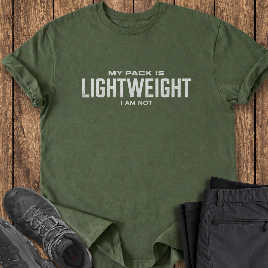 Green t-shirt with 'My pack is lightweight, I am not' text on a wooden surface with shoes and pants. funny backpacking hiking t shirt