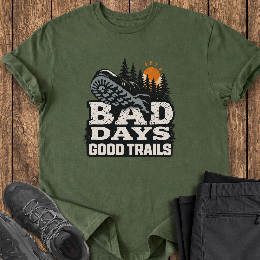 Green t-shirt with 'Bad Days Good Trails' graphic on a wooden surface with shoes and pants. bad day hiking t shirt
