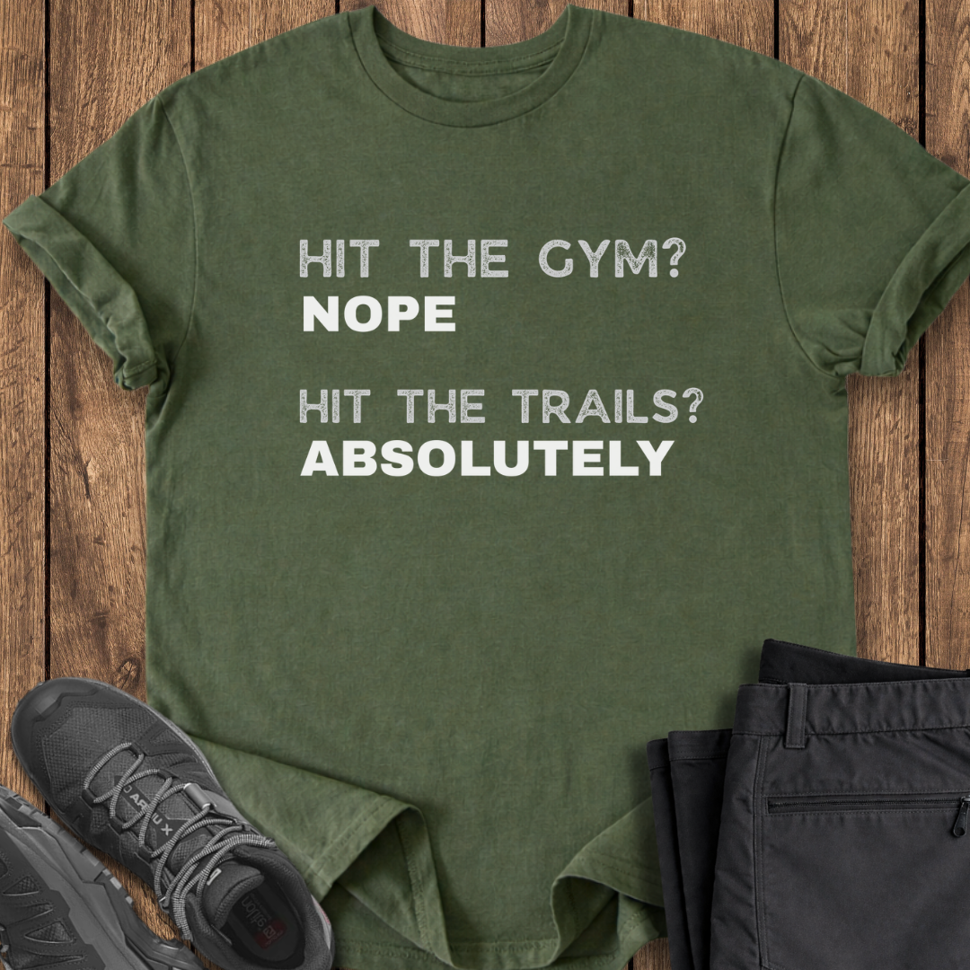 Green t-shirt with text 'Hit the gym? Nope, hit the trails? Absolutely' on a wooden surface with shoes and pants.