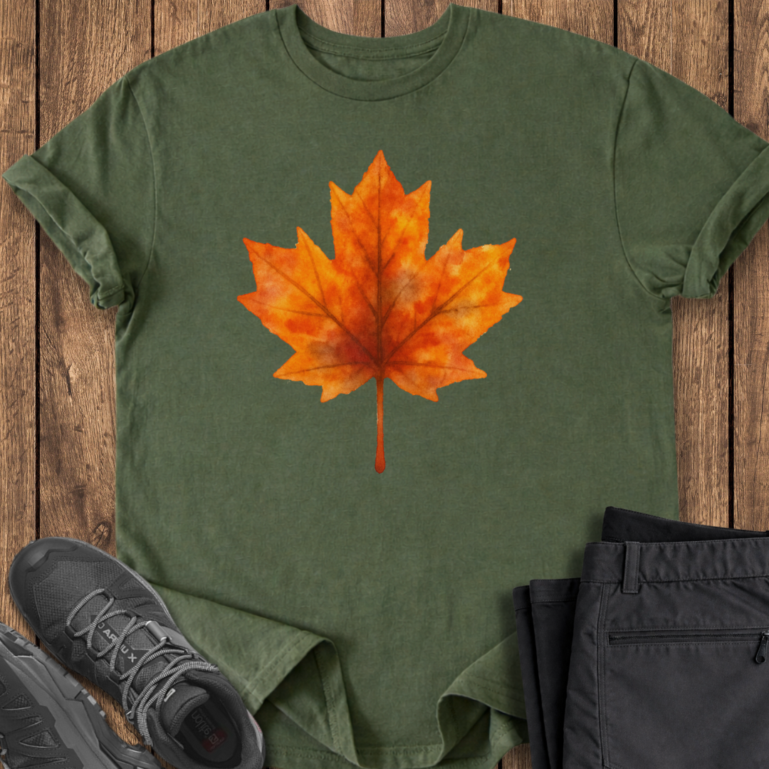Green t-shirt with orange maple leaf design on a wooden surface with shoes and pants.