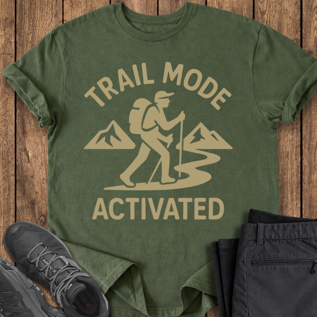 Green t-shirt with 'Trail Mode Activated' design on a wooden surface with hiking shoes and pants.