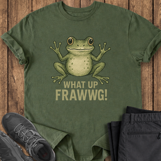 Green t-shirt with a frog graphic and text on a wooden surface, accompanied by black pants and shoes.