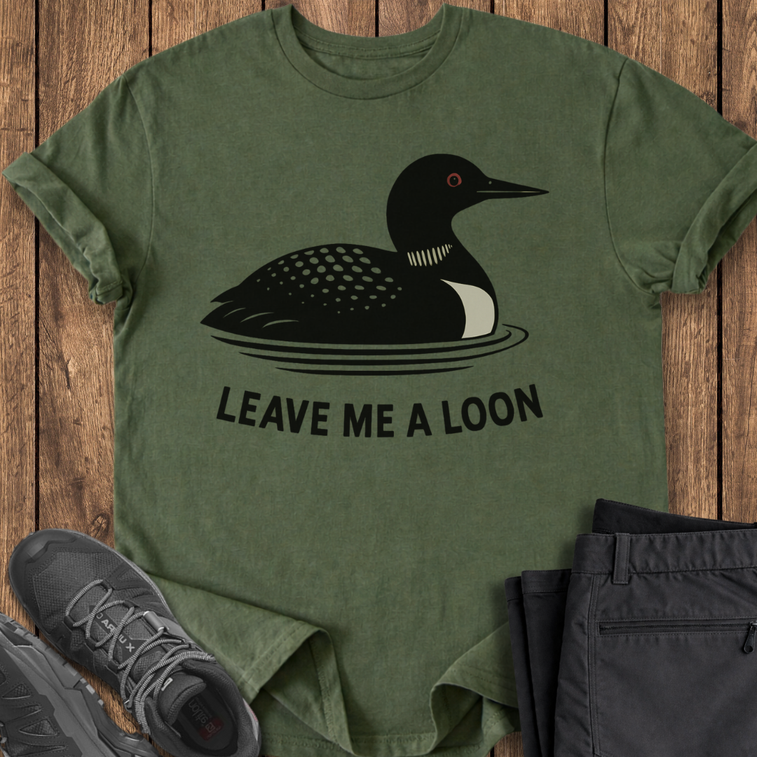 Green t-shirt with a duck graphic and 'Leave Me A Loon' text on a wooden surface, with shoes and pants partially visible.