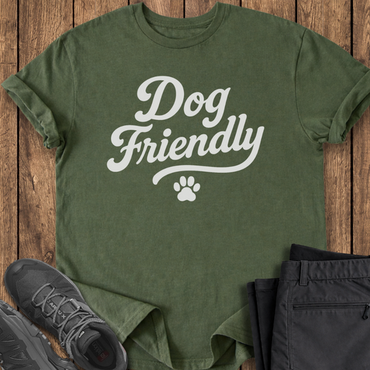 Green t-shirt with 'Dog Friendly' text on a wooden surface with shoes and pants.