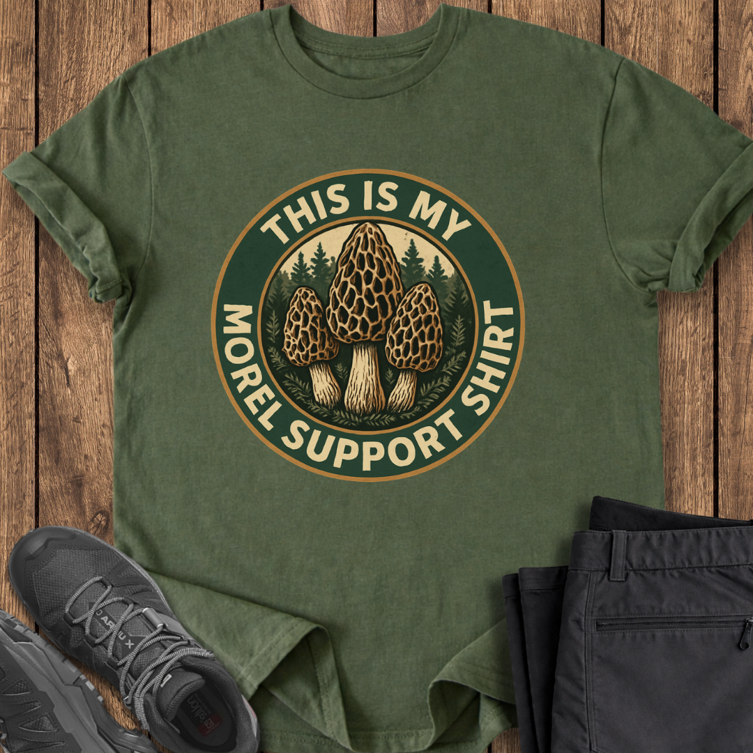 Green t-shirt with mushroom graphic and text on a wooden surface, accompanied by shoes and pants.