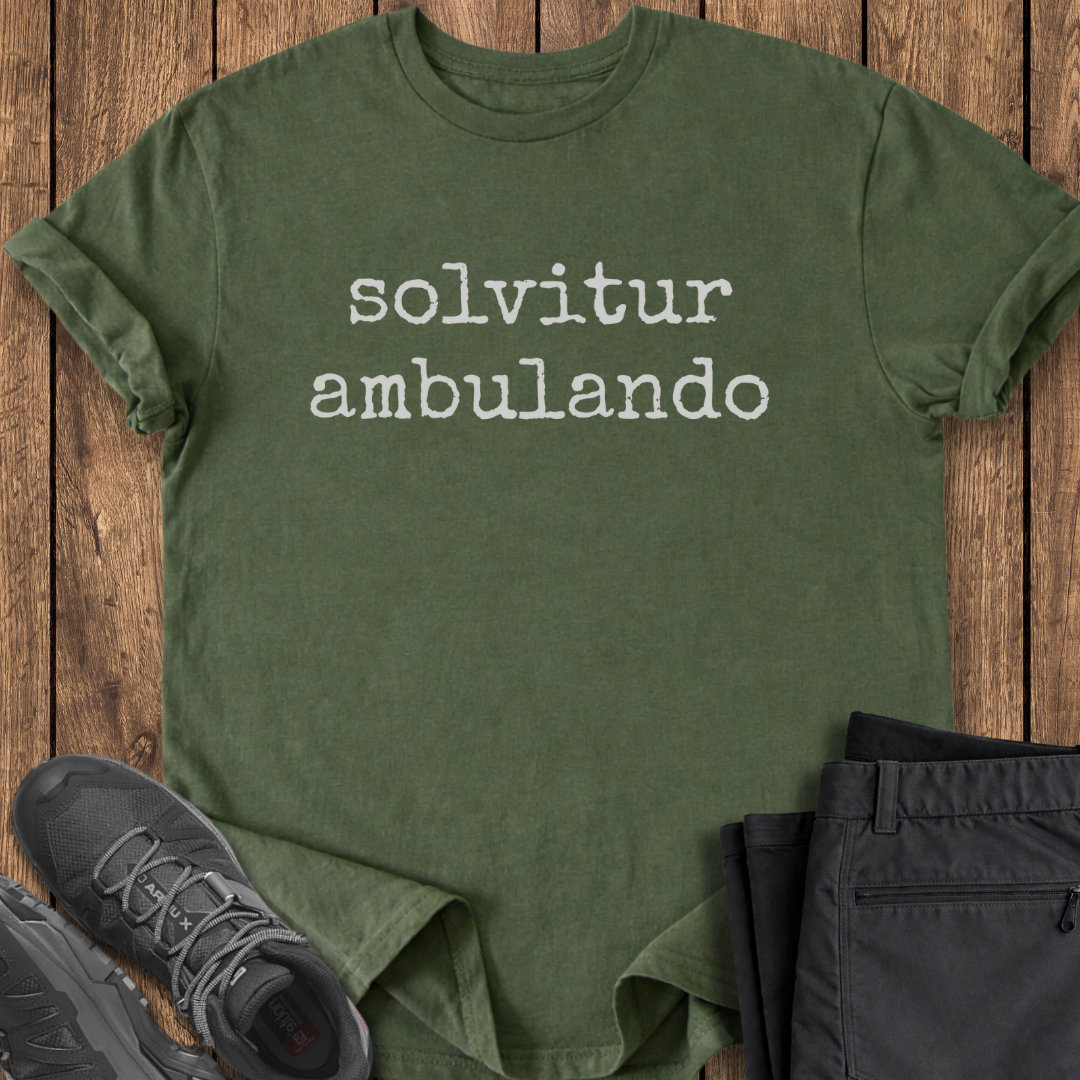 Green t-shirt with 'solvitur ambulando' text on a wooden surface with shoes and pants.