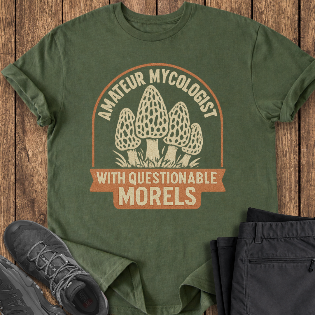 Green t-shirt with mushroom graphic and text on a wooden surface, accompanied by black shoes and pants.