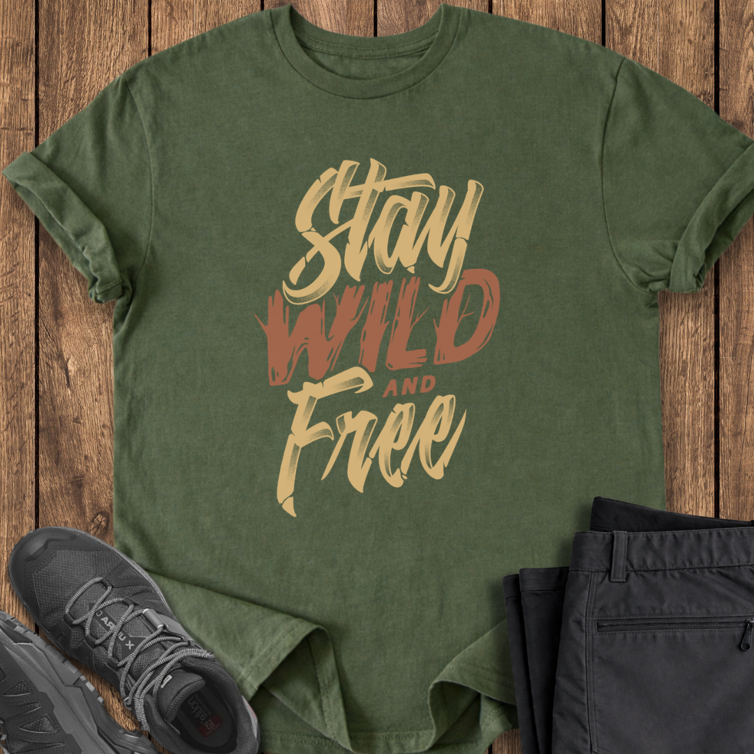 Green t-shirt with 'Stay Wild and Free' text on a wooden surface with shoes and pants.