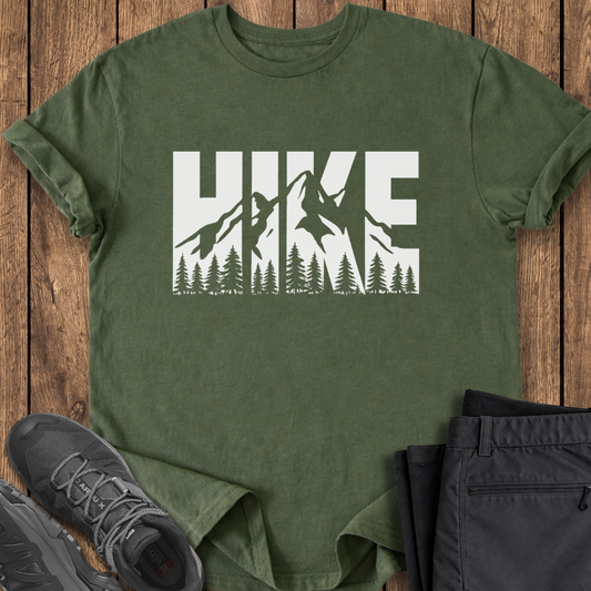 Green t-shirt with 'HIKE' graphic on a wooden surface with shoes and pants.