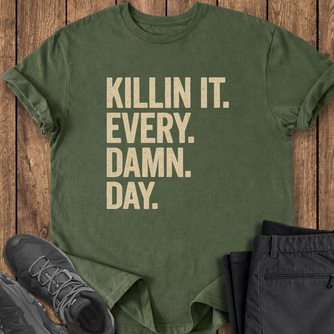 Green t-shirt with 'KILLIN IT. EVERY. DAMN. DAY.' text on a wooden surface with shoes and pants.