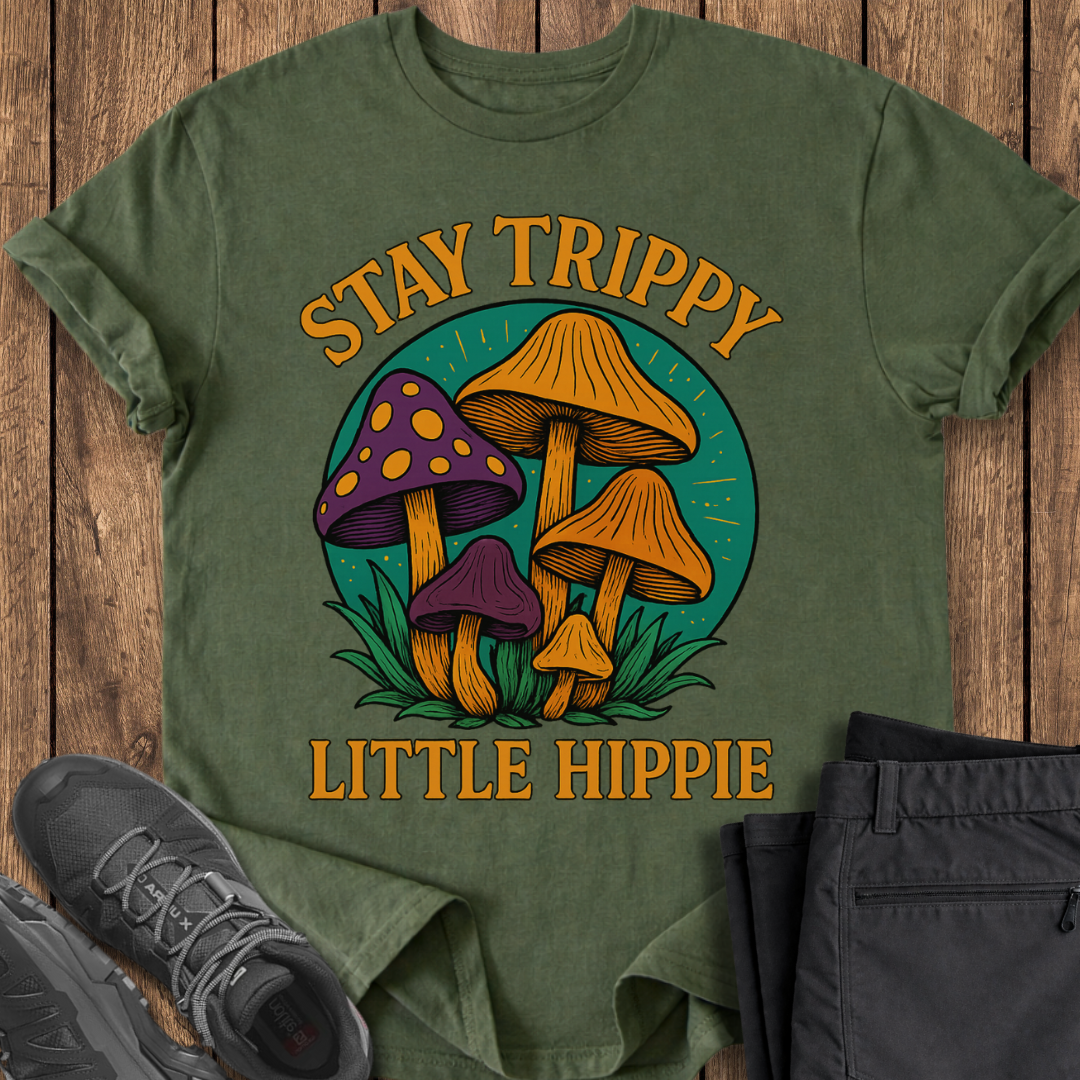 Green t-shirt with mushroom design and text 'Stay Trippy Little Hippie' on a wooden surface.