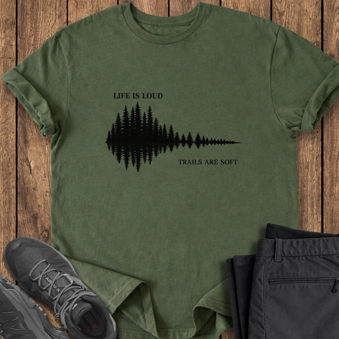 Green t-shirt with nature-themed design and text on a wooden surface with shoes and pants. mindful hiking t shirt