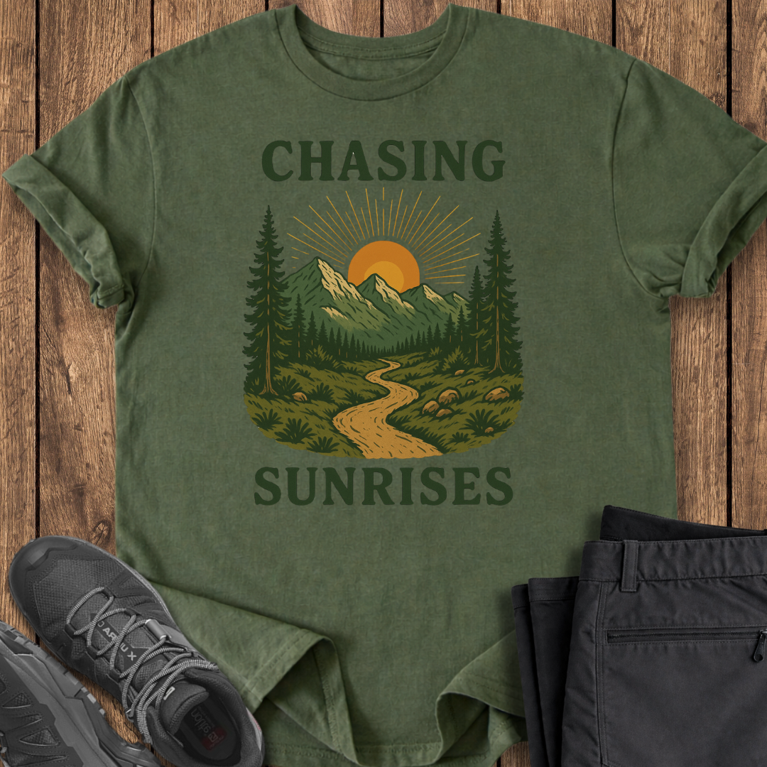 Green t-shirt with nature graphic and text 'Chasing Sunrises' on a wooden surface with shoes and pants.