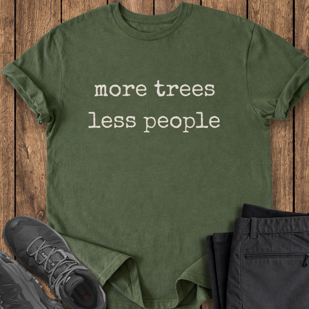 Green t-shirt with 'more trees less people' text on a wooden surface with shoes and pants.