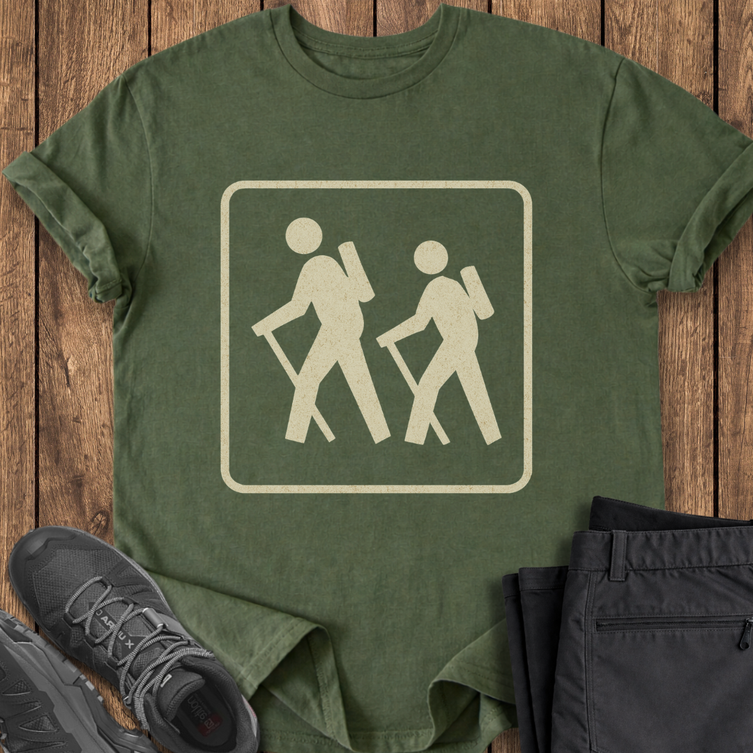 Green t-shirt with hiking icon on a wooden surface with shoes and pants. hiking backpacking vintage national park trail sign