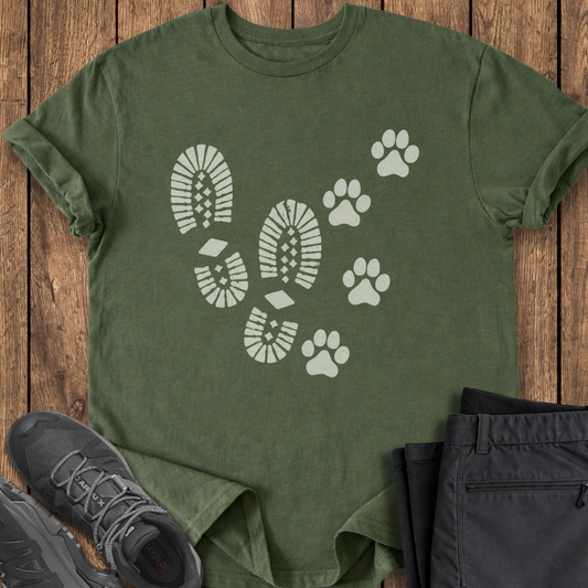 Green t-shirt with white paw print design on a wooden surface with black pants and shoes.