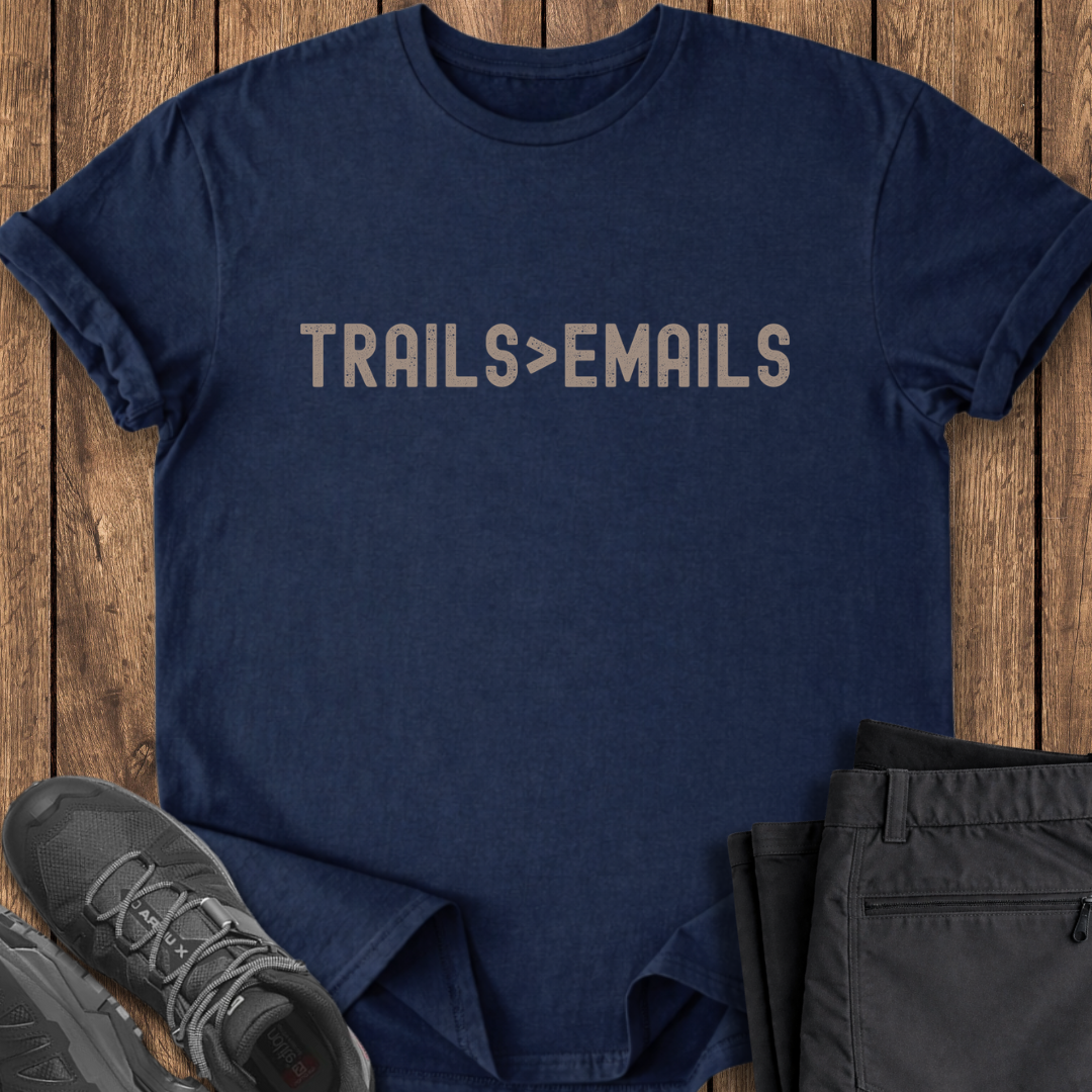 Navy blue t-shirt with 'TRAILS > EMAILS' text on a wooden surface with shoes and pants.